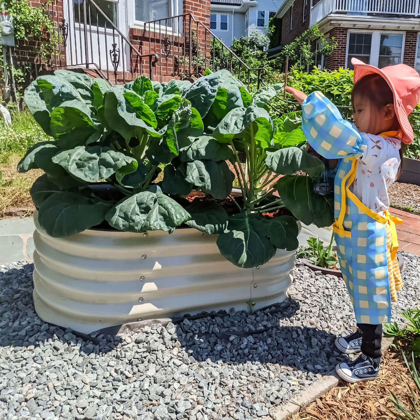 Child in a garden with the 17 inch tall kids first raised garden bed with leafy plants growing.
