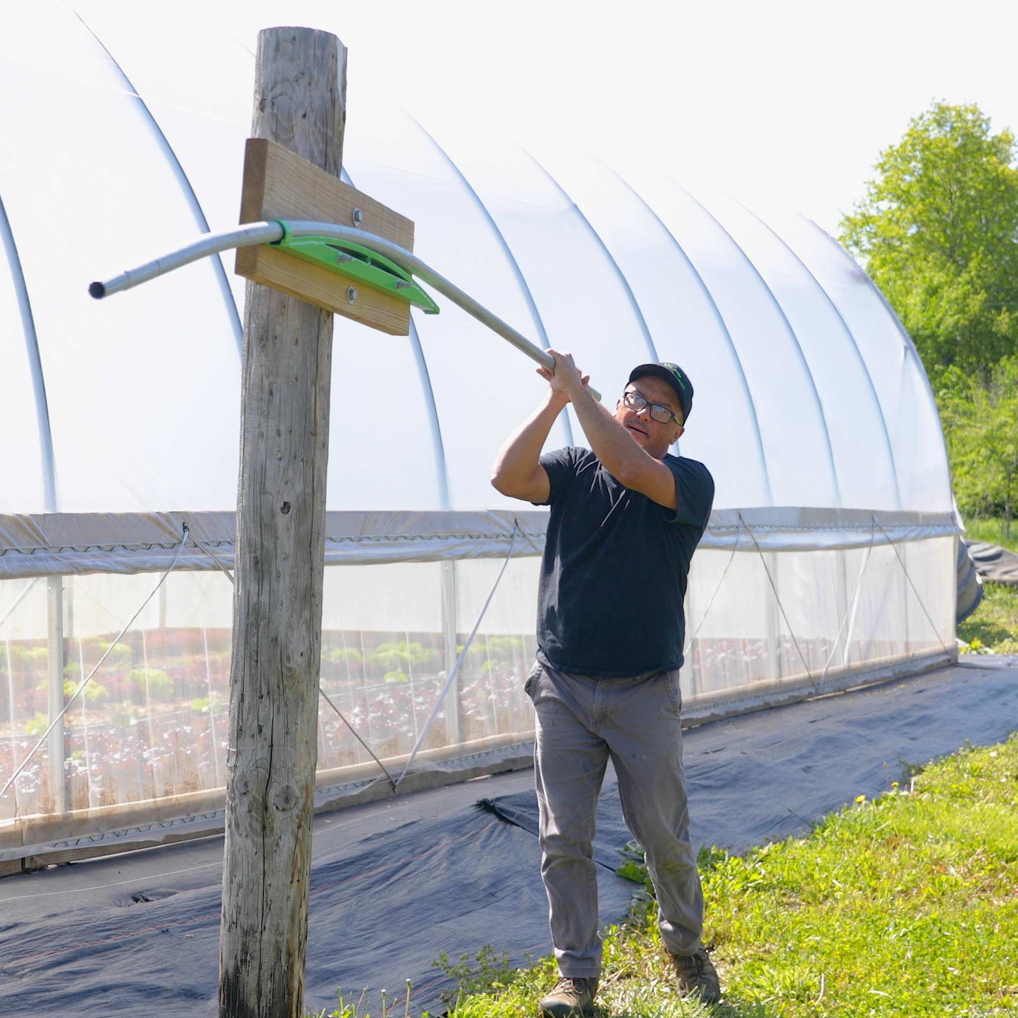 Person working with a hoop bender tool outside a greenhouse