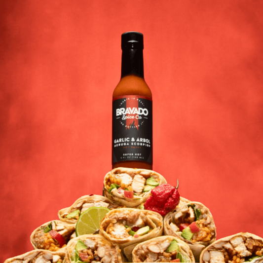 Garlic and Arbol Moruga Scorpion sauce bottle on a pyramid of burritos with scorpion peppers against a red background