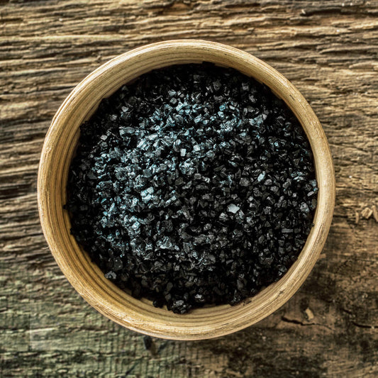 Wooden bowl filled with black sea salt on a wooden surface