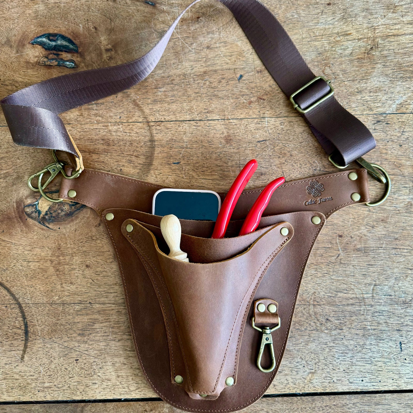 Brown leather tool belt with tools on a wooden surface