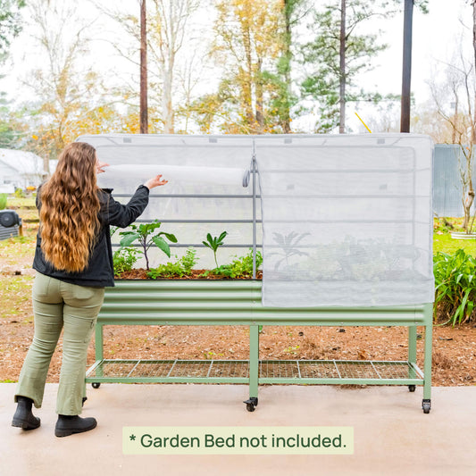 Person interacting with a green metal garden bed with a mesh cover in an outdoor setting with text clarifying the garden bed is not included.