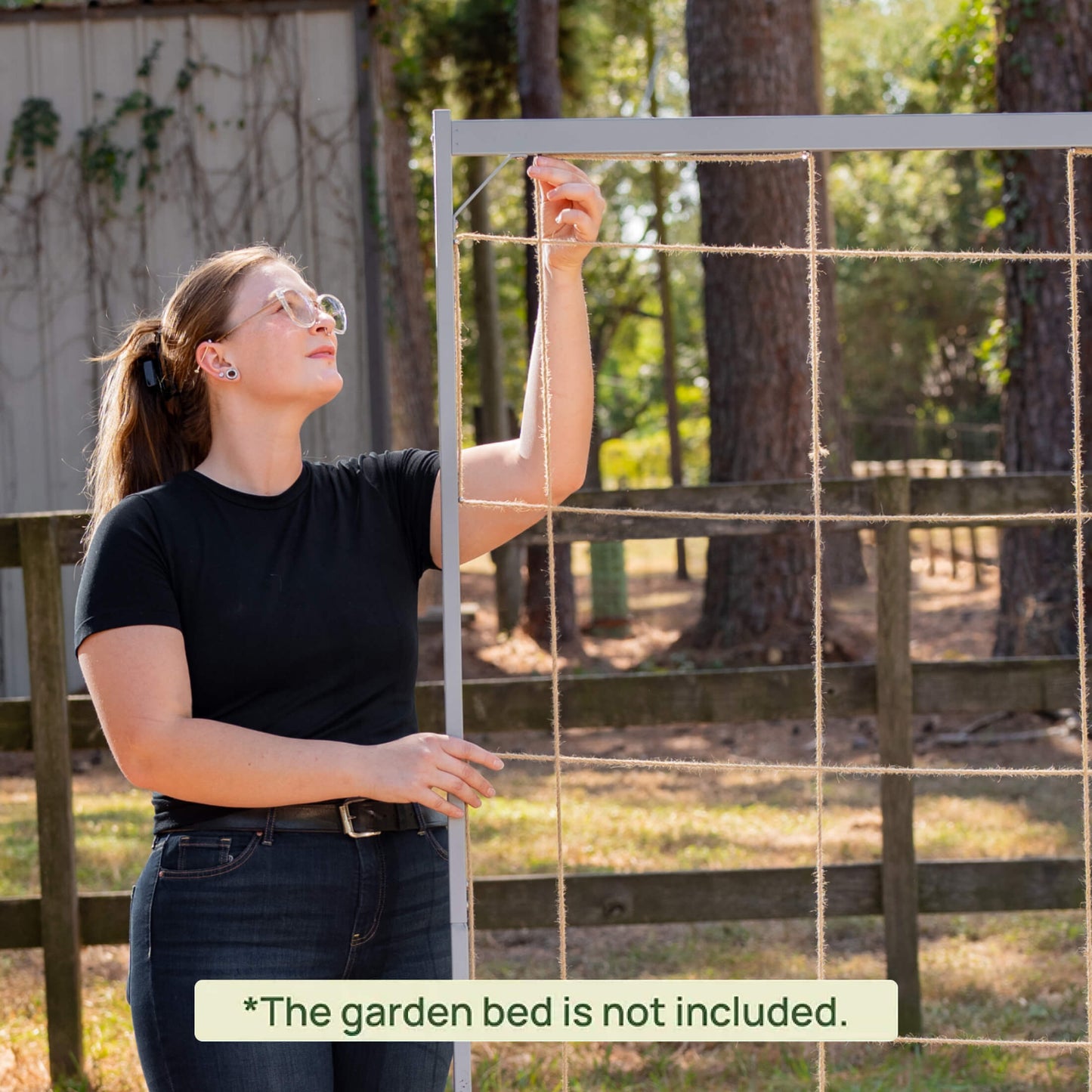 Person setting up a garden bed frame and string outdoors with trees in the background