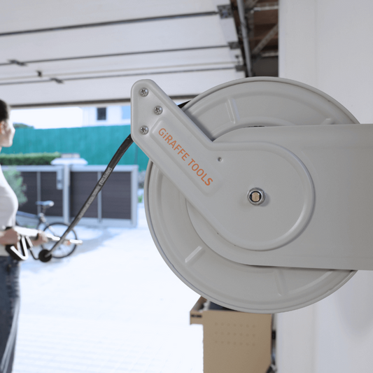 Retractable pressure hose reel installed on garage interior with a person unwinding the hose to use outside.