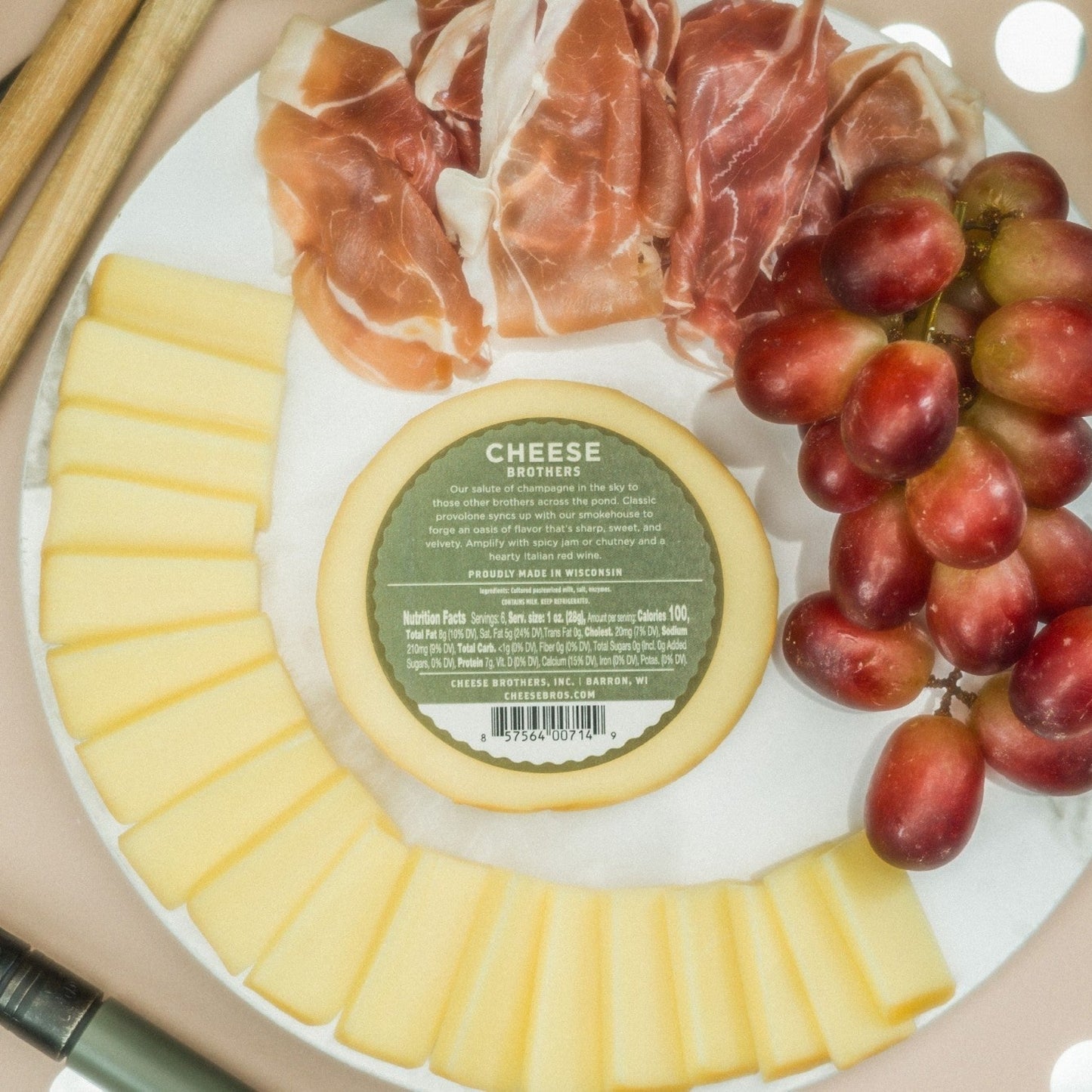 Smoked provolone cheese product label with ingredients and nutrition facts displayed on a serving platter with sliced cheese, deli meat, and grapes