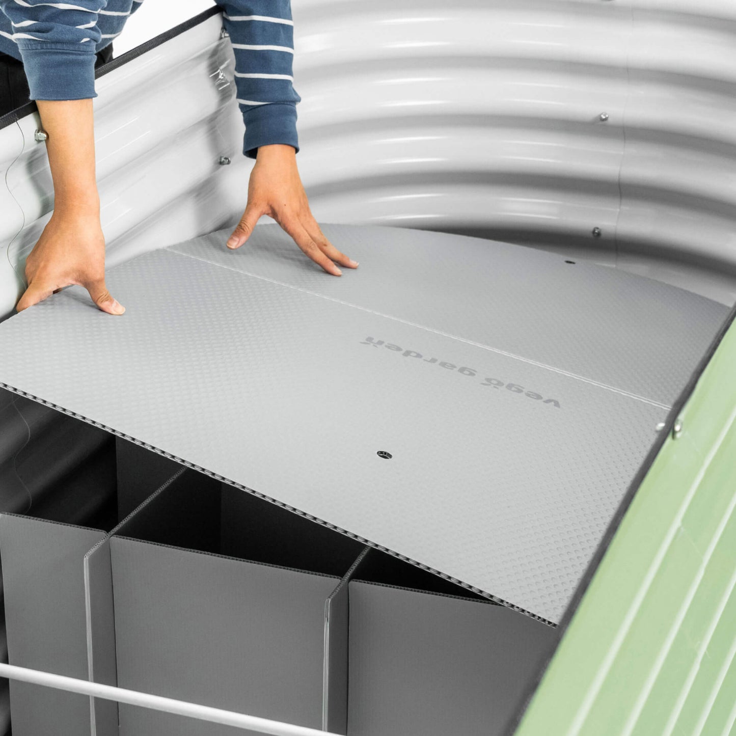 Person installing the top board soil partition onto the supports of the Soil Saving Floor into a 32 inch raised garden bed.