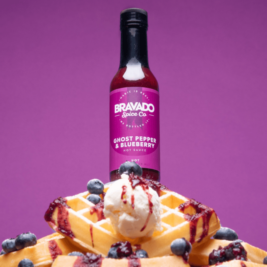 Ghost pepper blueberry hot sauce bottle on a waffle with ice cream and berries against a purple background