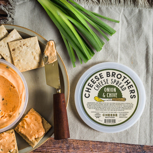 A cheese spreader with Onion and Chive Cheese Spread, accompanied by crackers and fresh chives on a wooden surface.