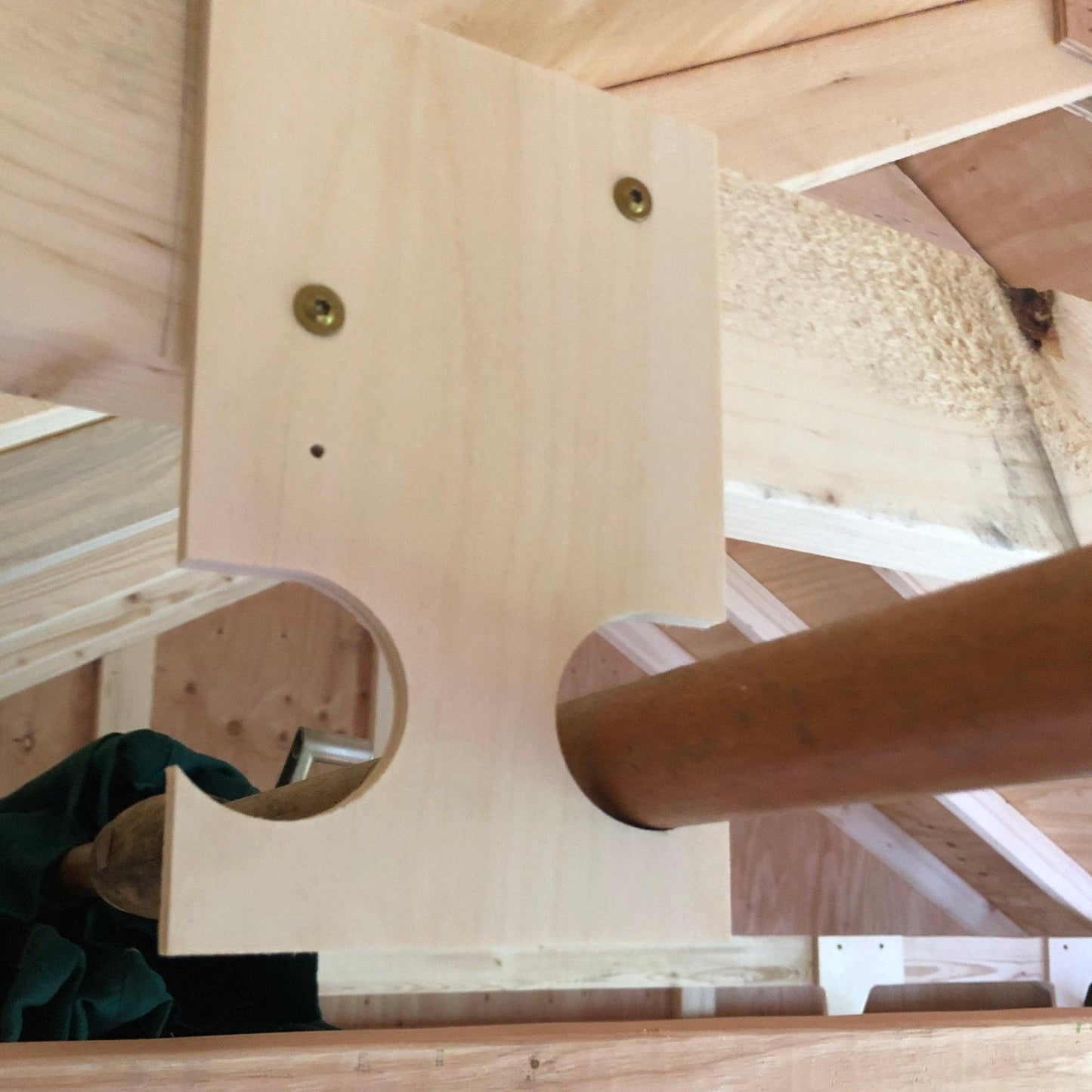Close-up of a pole saw and pool equipment organizer wood grain installed on a ceiling joist and a pole saw in the rack.