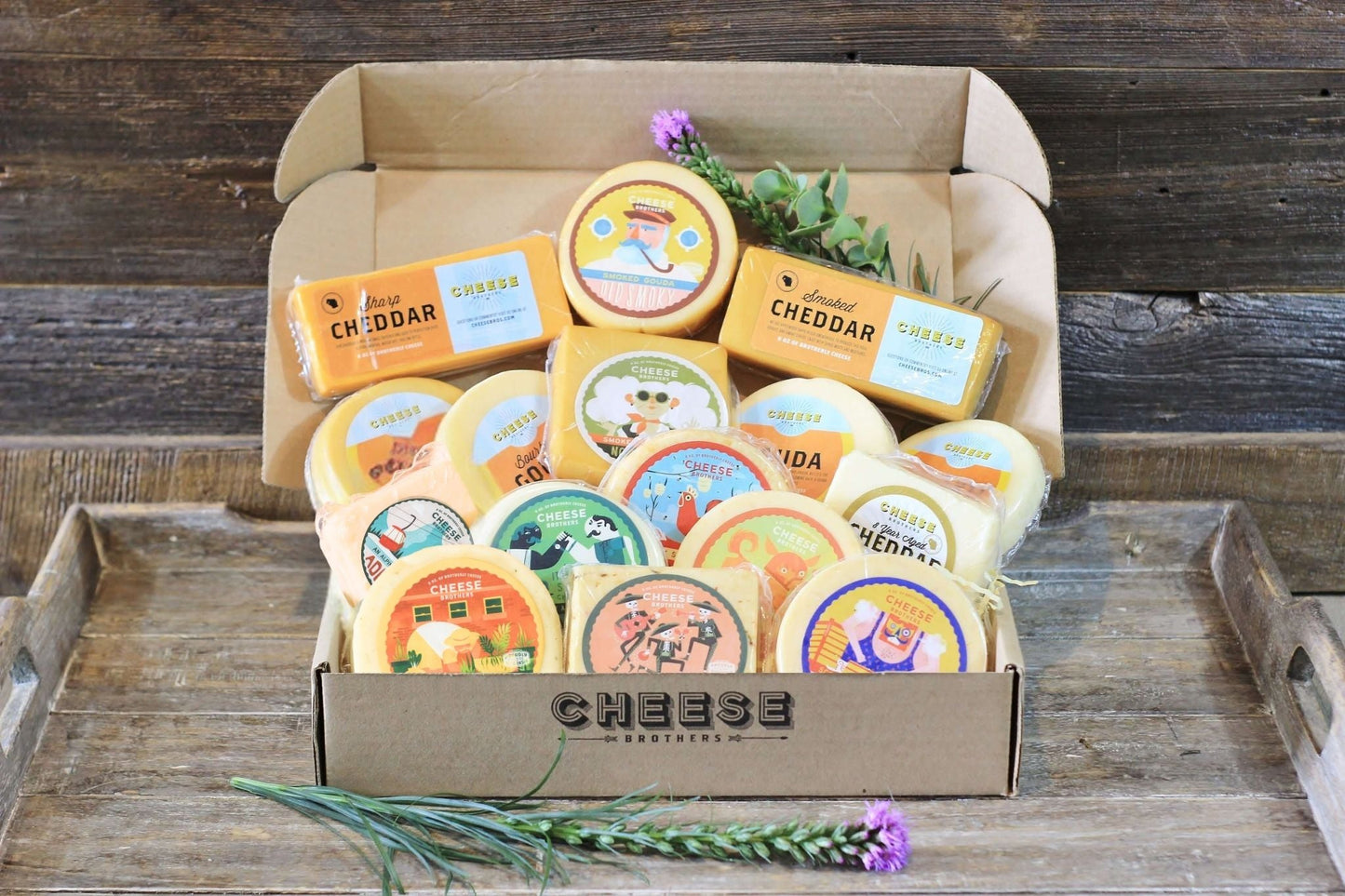 An assortment of cheese blocks presented inside box, including various flavors like gouda, havarti, and cheddar, with decorative elements like herbs and flowers.