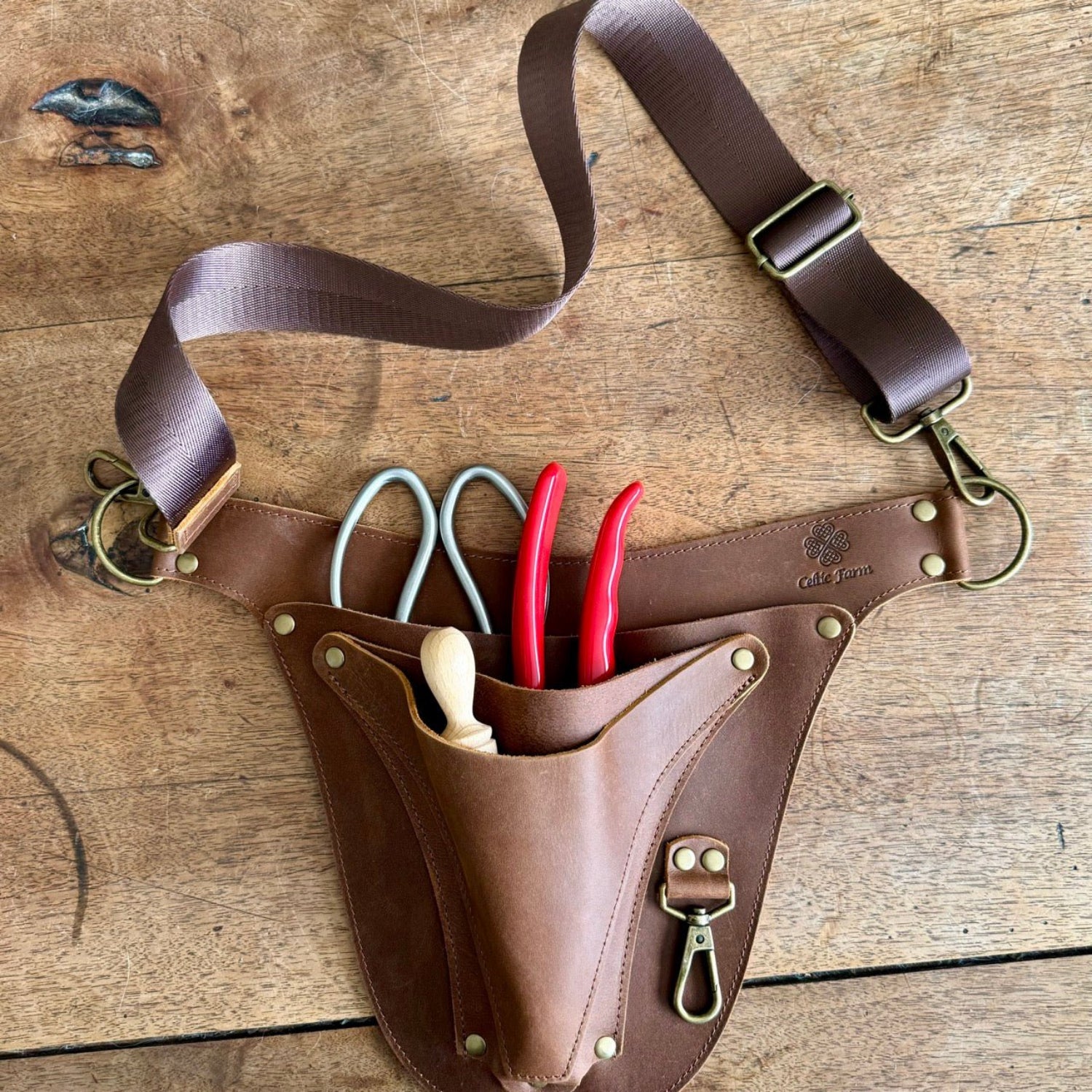 Brown leather tool belt with tools on a wooden surface