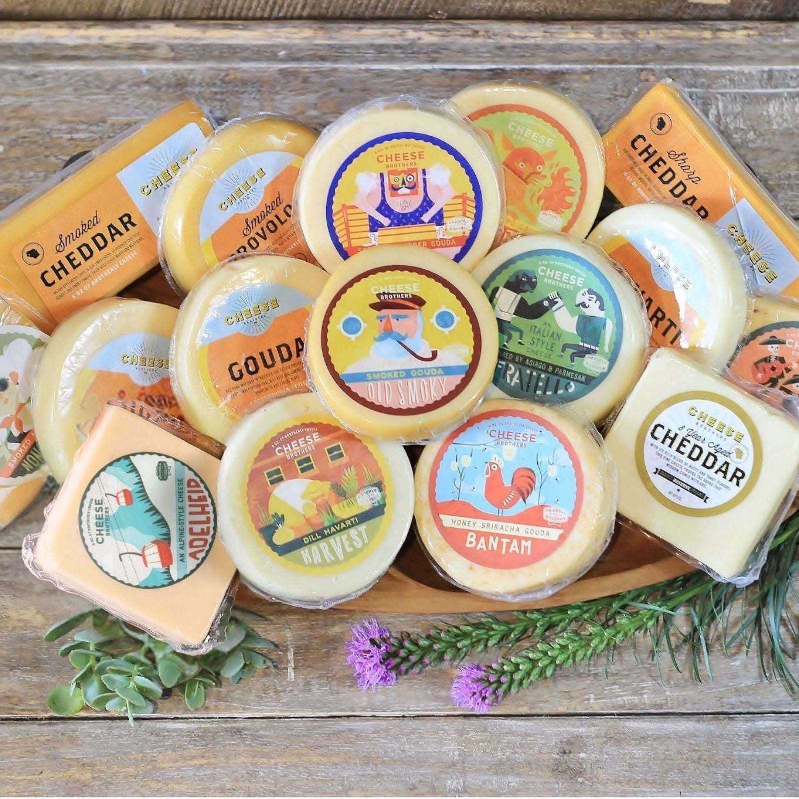 An assortment of cheese blocks presented on a wooden surface, including various flavors like gouda, havarti, and cheddar, with decorative elements like herbs and flowers.