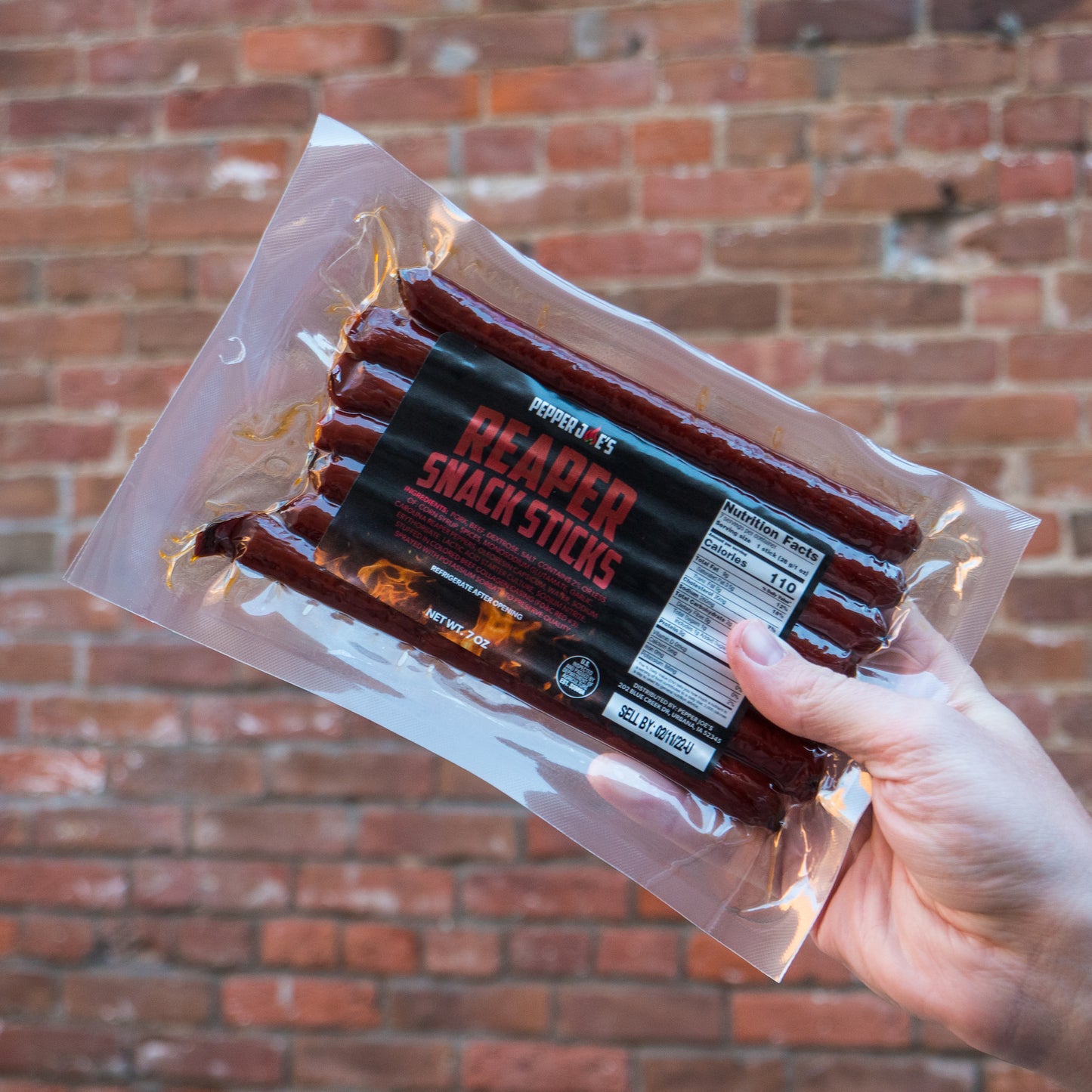 Pepper Joe's Carolina Reaper Snack Sticks - holding packaging behind brick wall