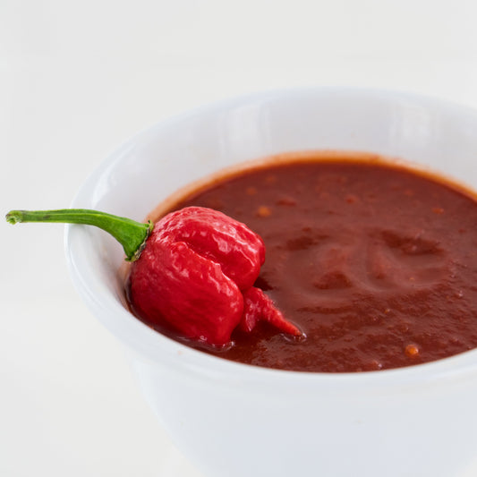 Carolina Reaper pepper resting in a bowl of fresh Carolina Reaper mash on a white background