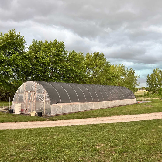 Long greenhouse structure on a grassy area with trees in the background