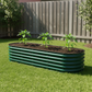 British green planter in backyard with three young pepper plants growing in it.