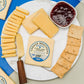 8 year aged cheddar presented on cutting board with decorative elements such as sliced cheese, crackers, jelly, and cheese spreader