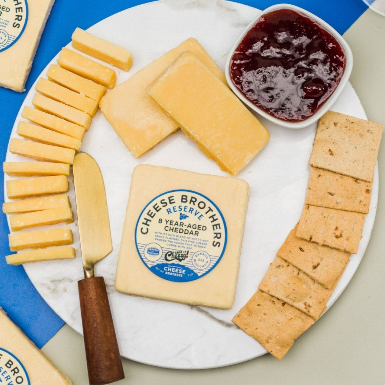 8 year aged cheddar presented on cutting board with decorative elements such as sliced cheese, crackers, jelly, and cheese spreader