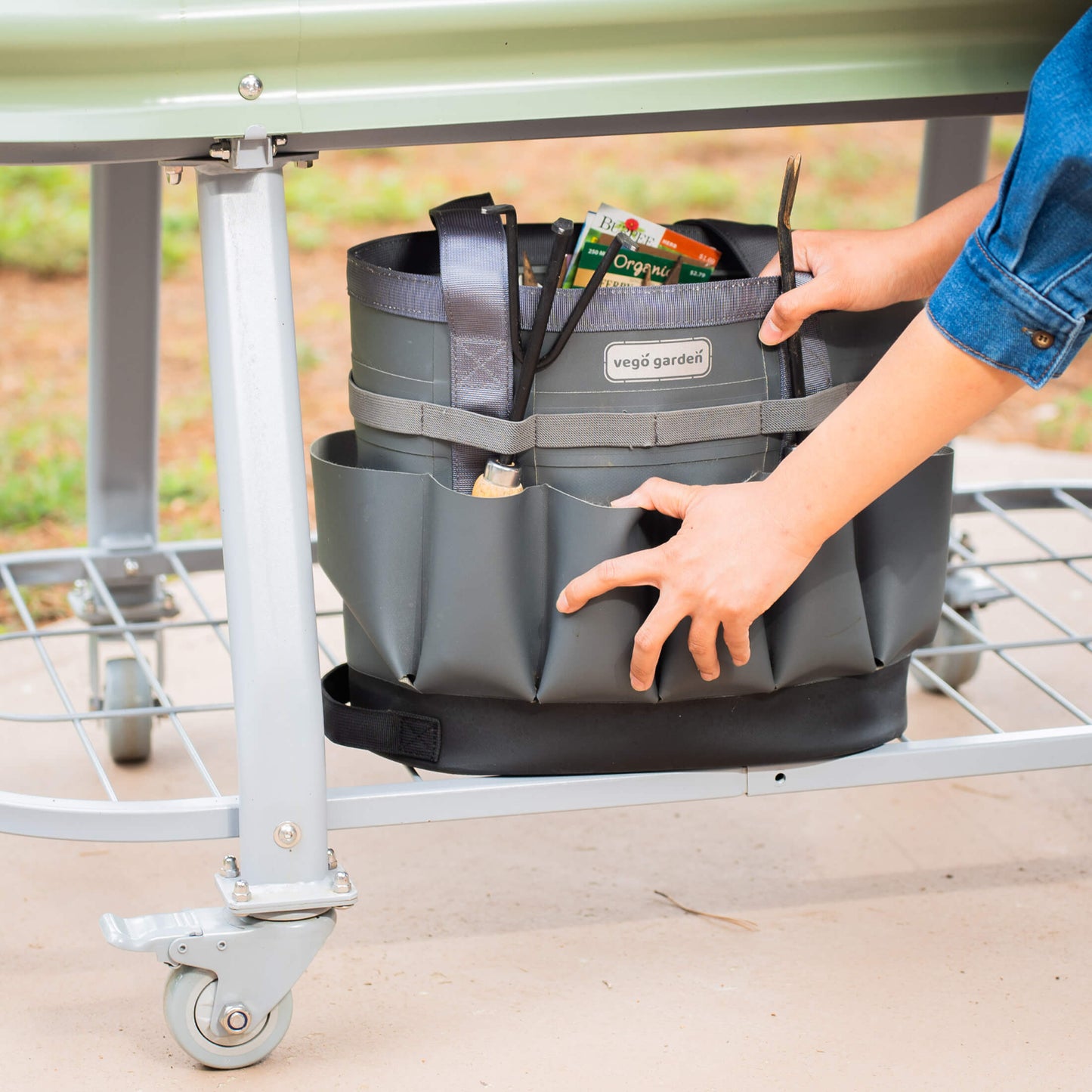 Pearl White elevated metal garden bed with wheels and self watering system zoomed in on the storage shelf under the bed with a garden bag full of supplies sitting on it.