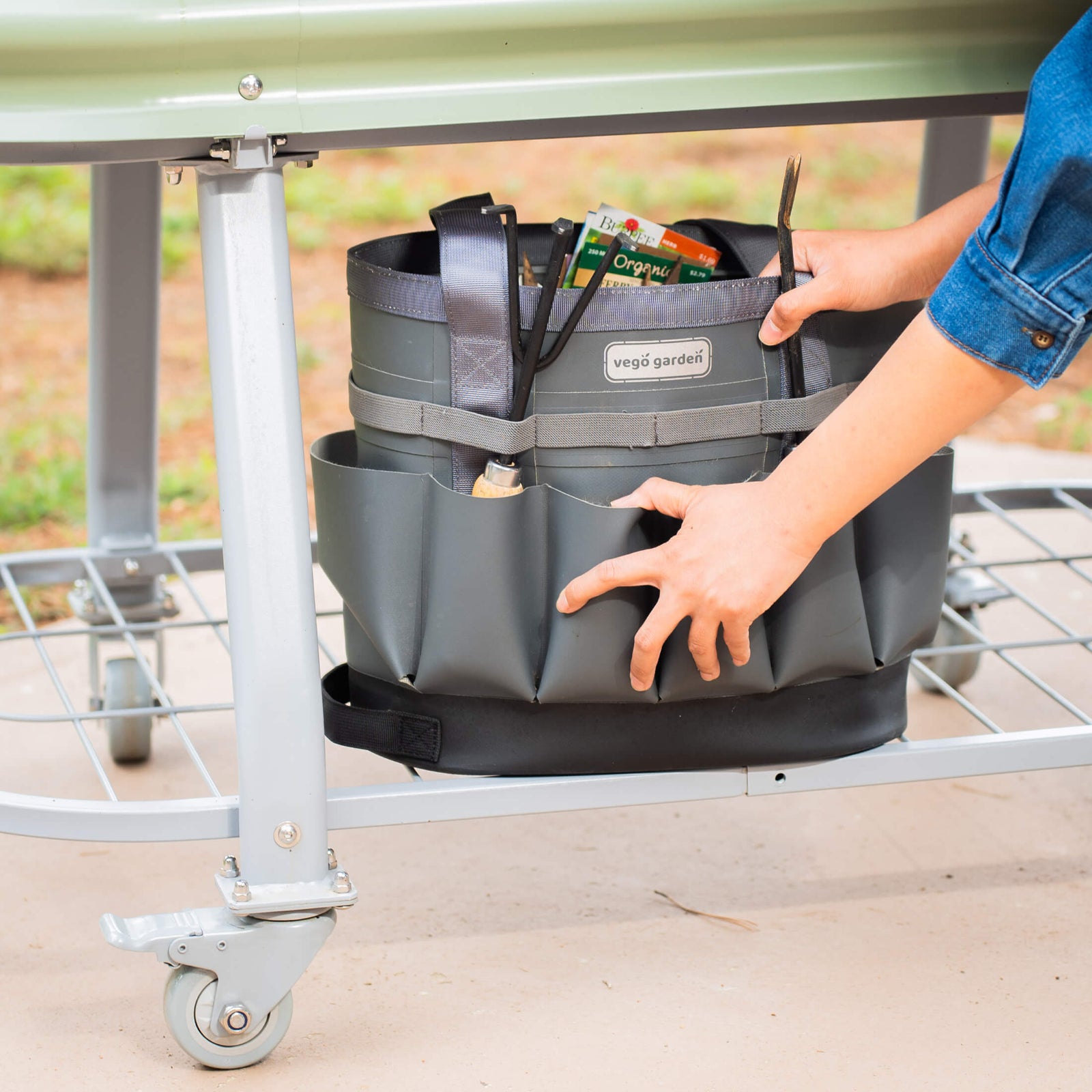 Pearl White elevated metal garden bed with wheels and self watering system zoomed in on the storage shelf under the bed with a garden bag full of supplies sitting on it.