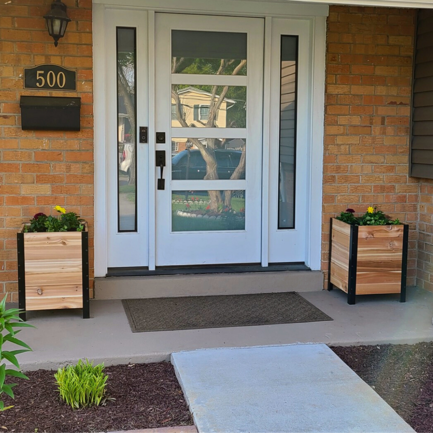 Two 18x18 inch planter boxes filled with colorful flowers on a front porch