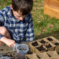 Child planting seeds in biodegradable seed starting pots with soil and water
