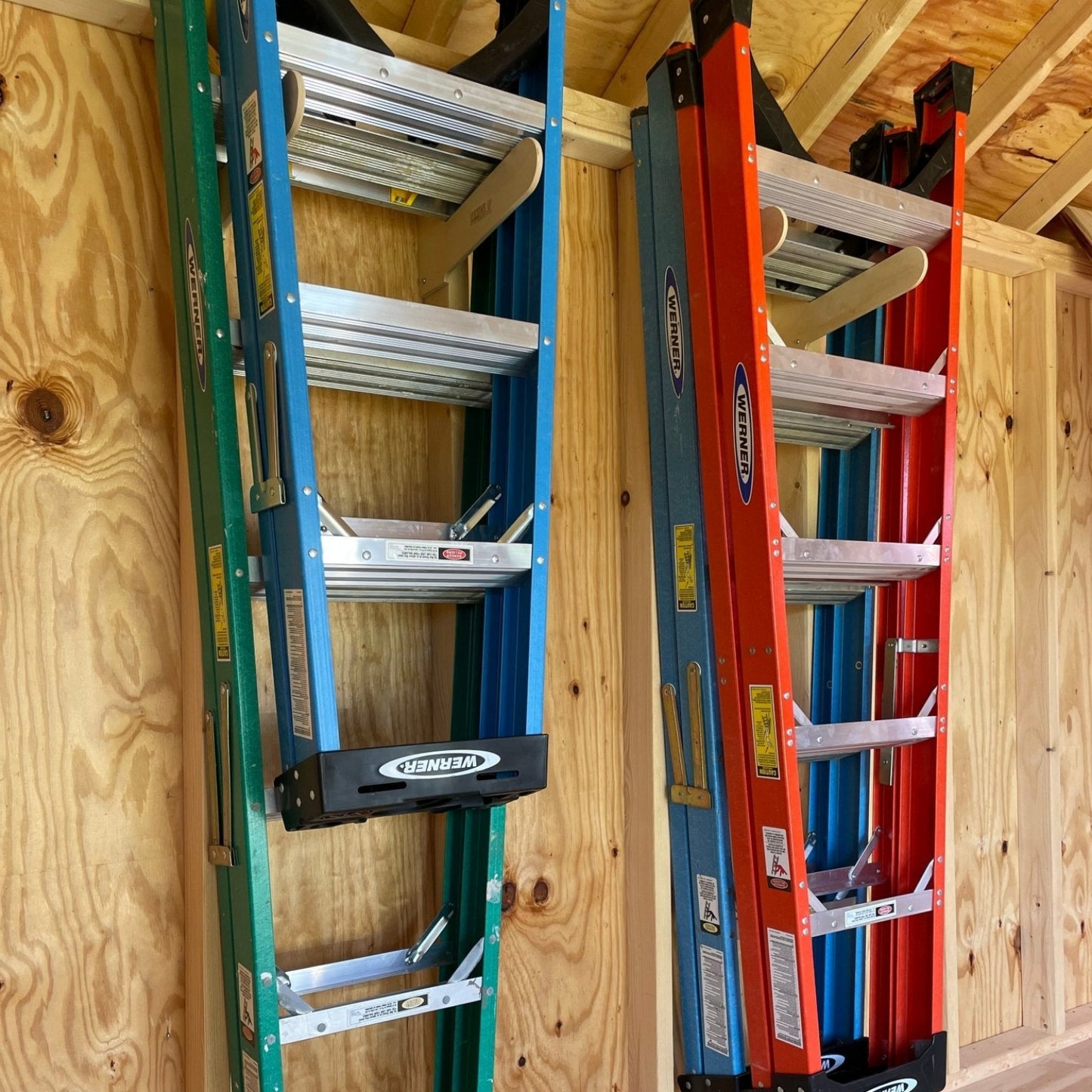 Two pairs of Step Ladder Organizers installed on an unfinished shed wall with step ladders hanging neatly.