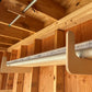 One pair of the storage organizer racks installed on an unfinished shed wall with a PVC pipe and metal gutter stored neatly in the rack. 