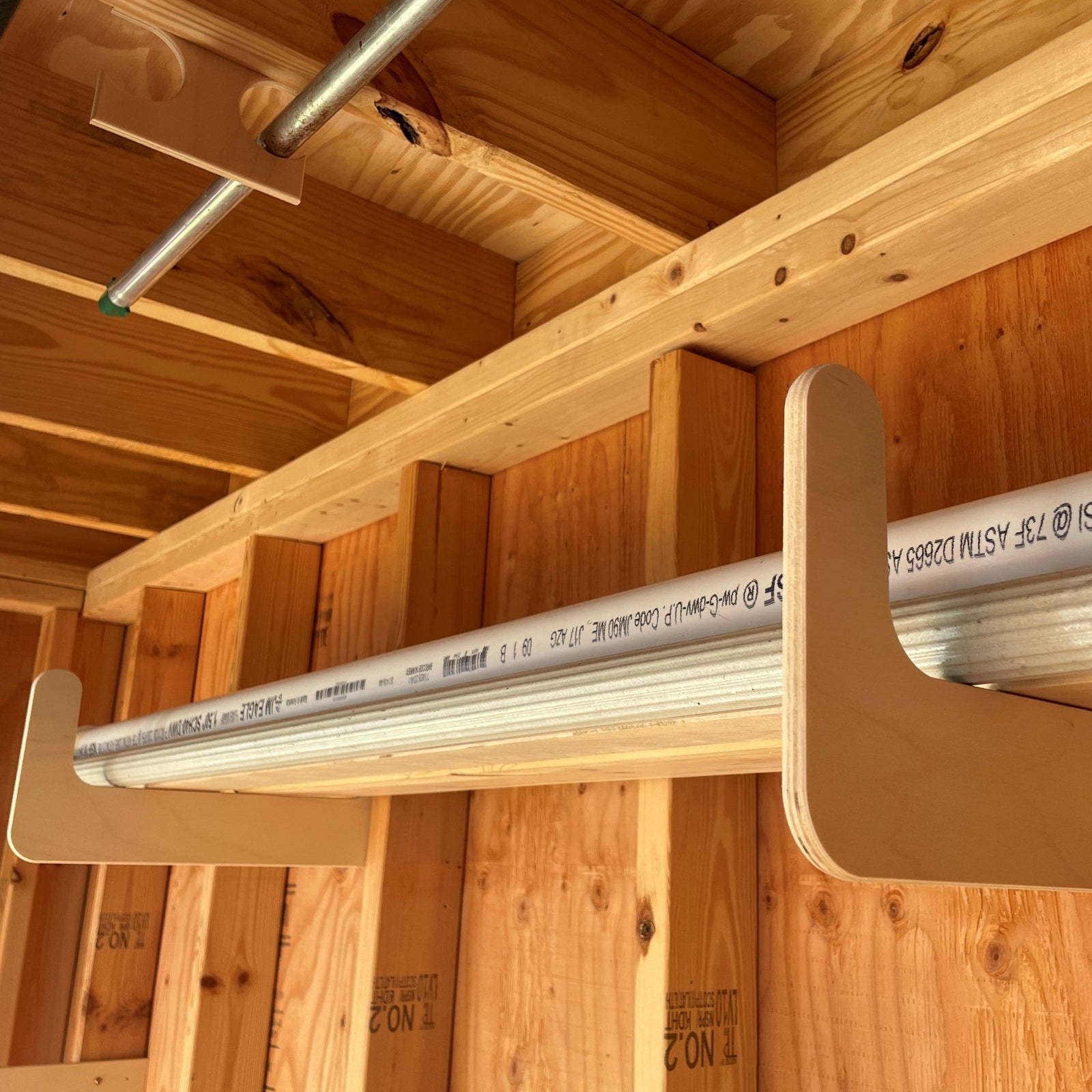 One pair of the storage organizer racks installed on an unfinished shed wall with a PVC pipe and metal gutter stored neatly in the rack. 