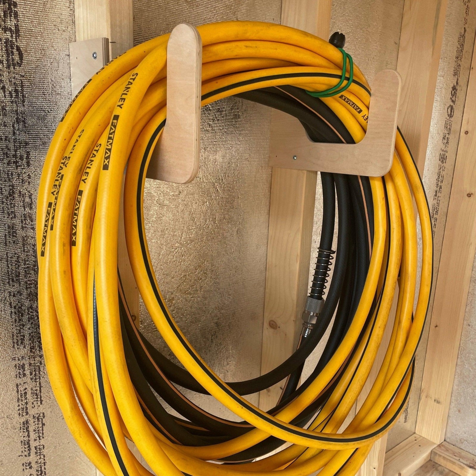 One pair of Hose/Extension Cord Organizer racks installed on an unfinished shed wall with hoses neatly hanging. 