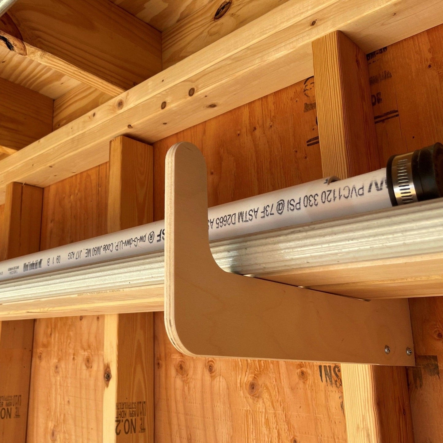 One pair of the storage organizer racks installed on an unfinished shed wall with PVC pipe and metal gutters stored neatly in the rack. 