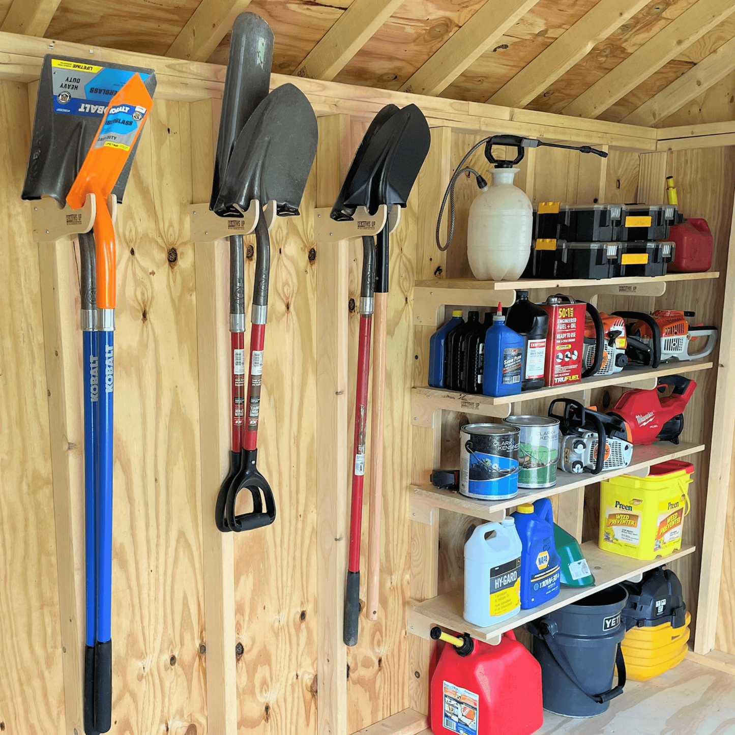 Garden tools and equipment organized on shelf and hooks hanging on the wall inside an unfinished shed.