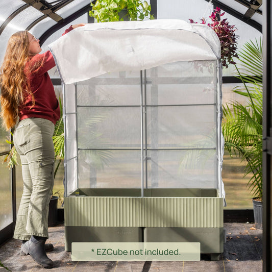 Person setting up the EZCube Cover System on an EZCube Self-Watering Planter inside a greenhouse.