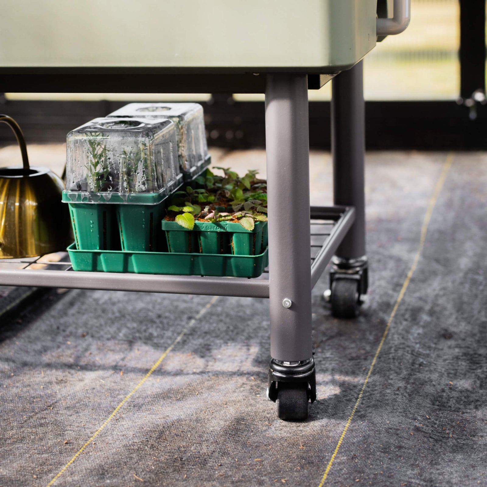 EZCube Elevated Rolling Planter Cart with a close up of the heavy0duty caster wheels and the built-in storage rack with seed starting supplies stored on it.