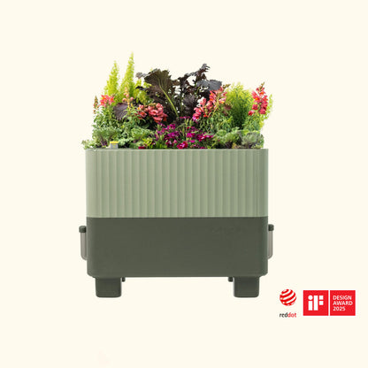 EZCube Self-Watering Planter – 21″ x 24″ in sage green with colorful flowers and plants on a white background.