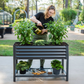 Person tending to pepper plants in a modern gray raised garden bed outdoors.