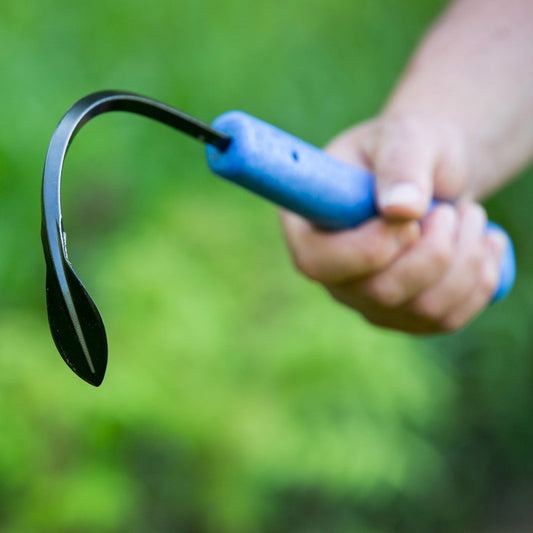 Hand holding a Full-Size Weeder & Cultivator Hand Tool against a green blurred background