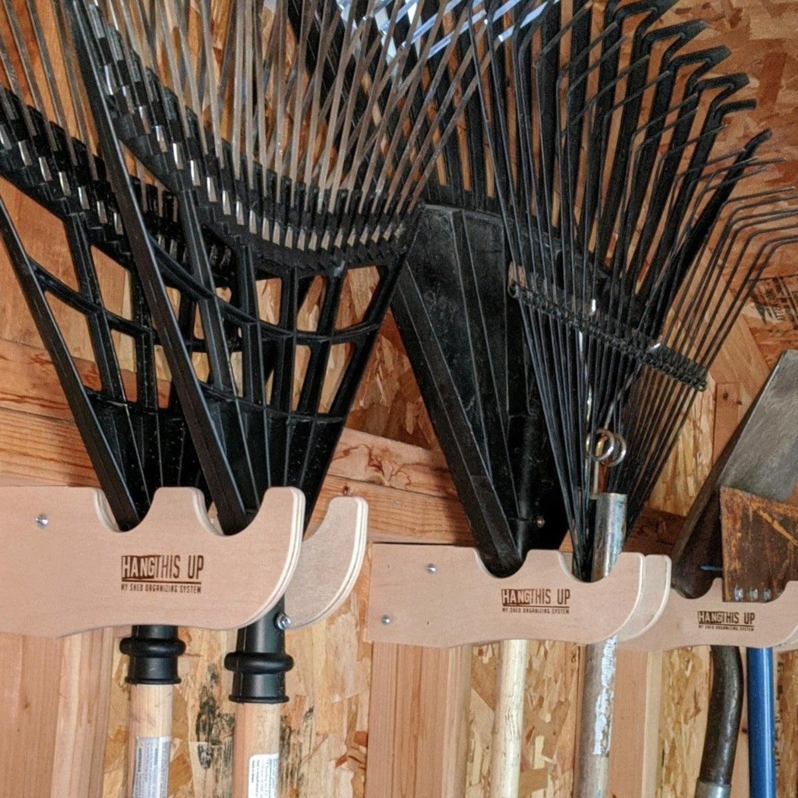Close-up of a garden yard tool organizer installed on the stud and yard rakes hanging on the organizers.