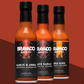 Three bottles of hot sauce on a brown gradient background with Garlic & Arbol Moruga Scorpion, Black Garlic Carolina Reaper, and AKA Miso Ghost Reaper flavors.
