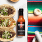 Garlic & Arbol Moruga Scorpion  hot sauce bottle with tacos and a colorful blanket in the background
