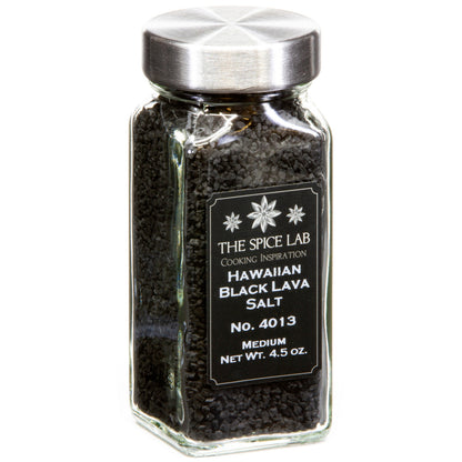 A glass spice jar filled with black lava salt, featuring a silver metal lid and a black label with white text that reads 'THE SPICE LAB HAWAIIAN BLACK LAVA SALT'.