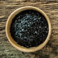 Wooden bowl filled with black sea salt on a wooden surface