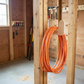 Stud-mounted utility organization rack holding an orange extension cord inside an unfinished shed wall.