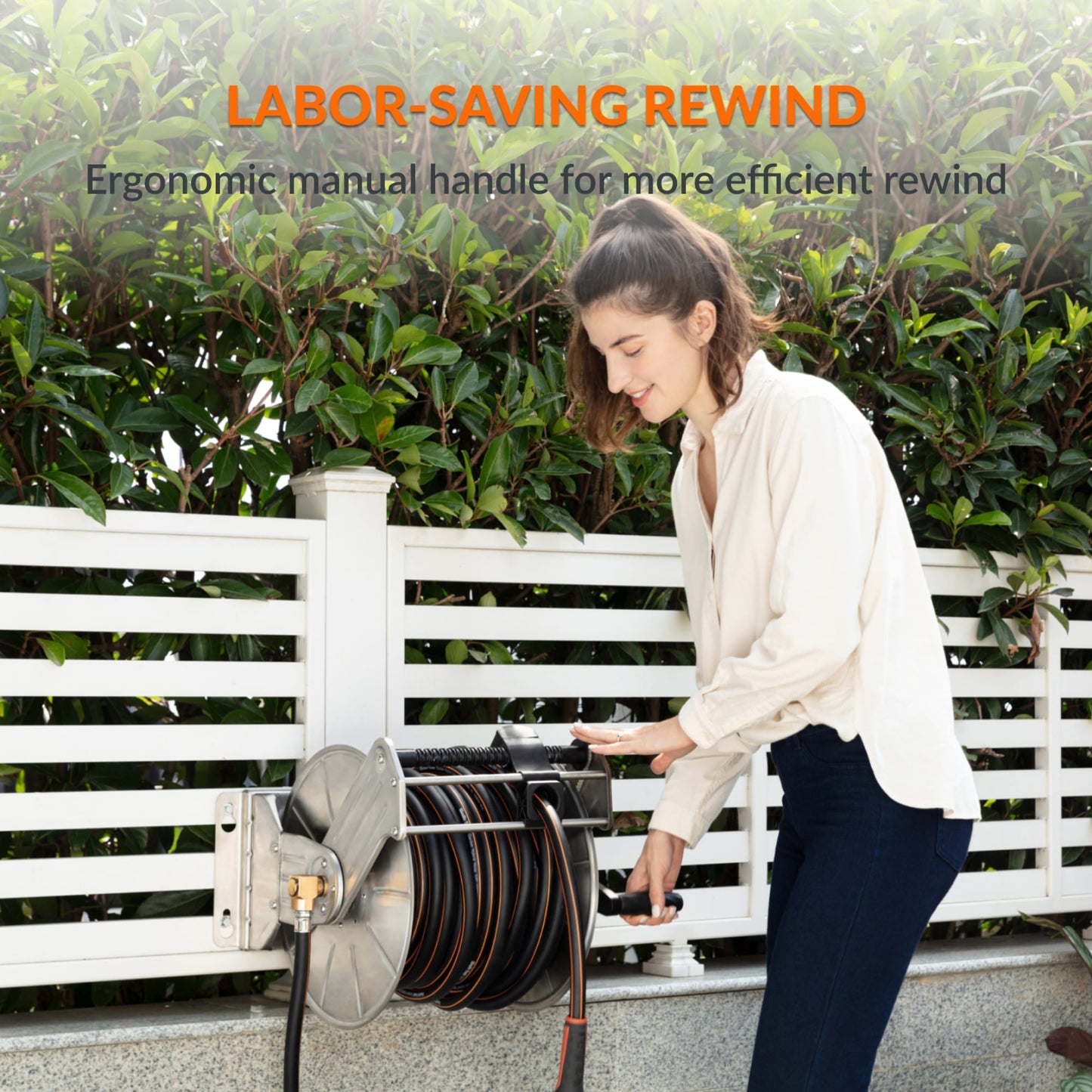 Woman using the ergonomic manual handle to rewind the heavy-duty wall-mounted stainless steel garden hose reel.  