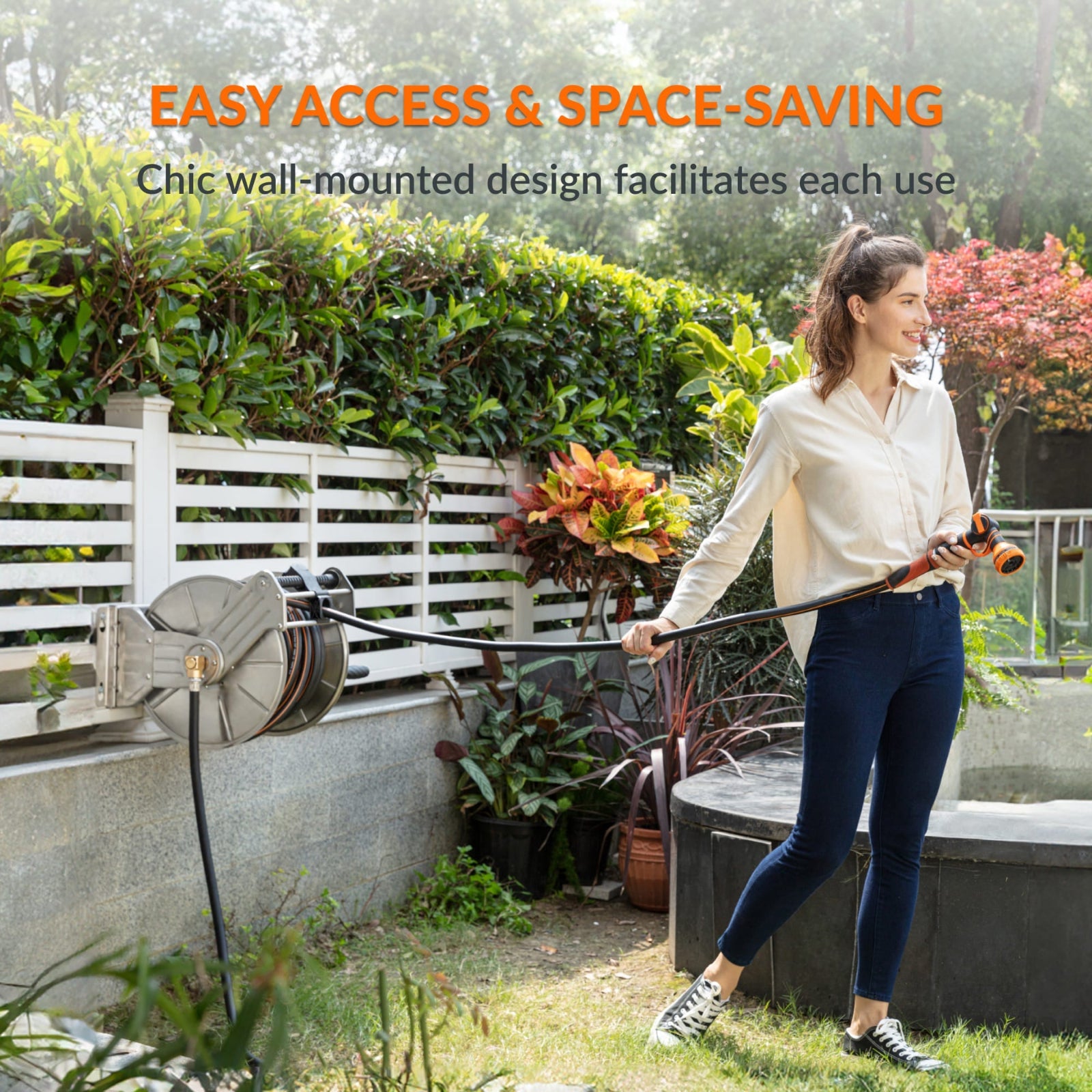 Woman holding a garden hose stored in the heavy-duty wall-mounted  stainless steel hose reel in a garden setting with text outlining easy access and space saving. 