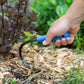 Hand holding a Mini Weeder & Cultivator Hand Tool in a garden setting removing weeds.