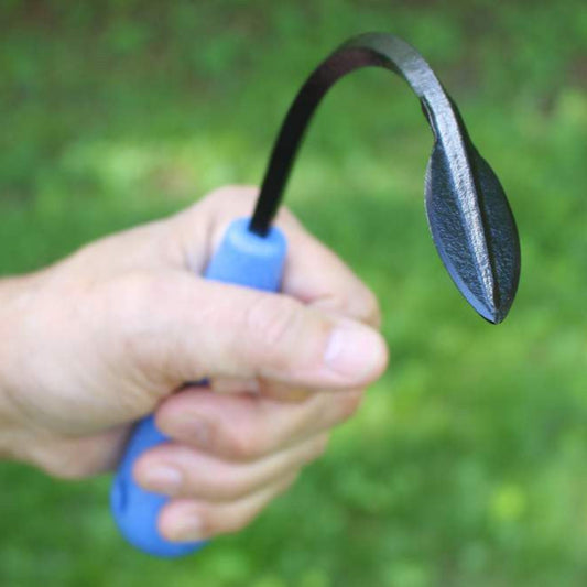 Hand holding a Mini Weeder and Cultivator hand tool with a curved blade against a blurred green background