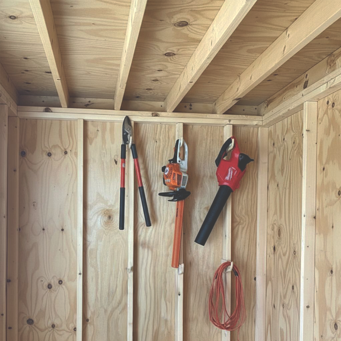 Stud-mounted miscellaneous hook organizers holding multiple yard tools neatly organized inside an unfinished shed.