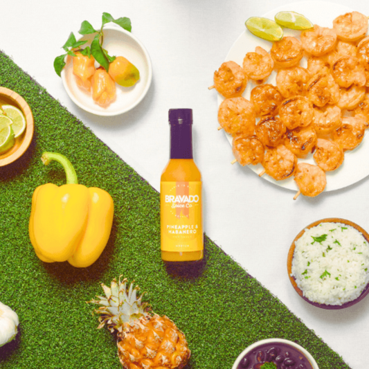 Pineapple & habanero sauce bottle with shrimp, pineapple, bell pepper, habanero peppers, and rice on a white background