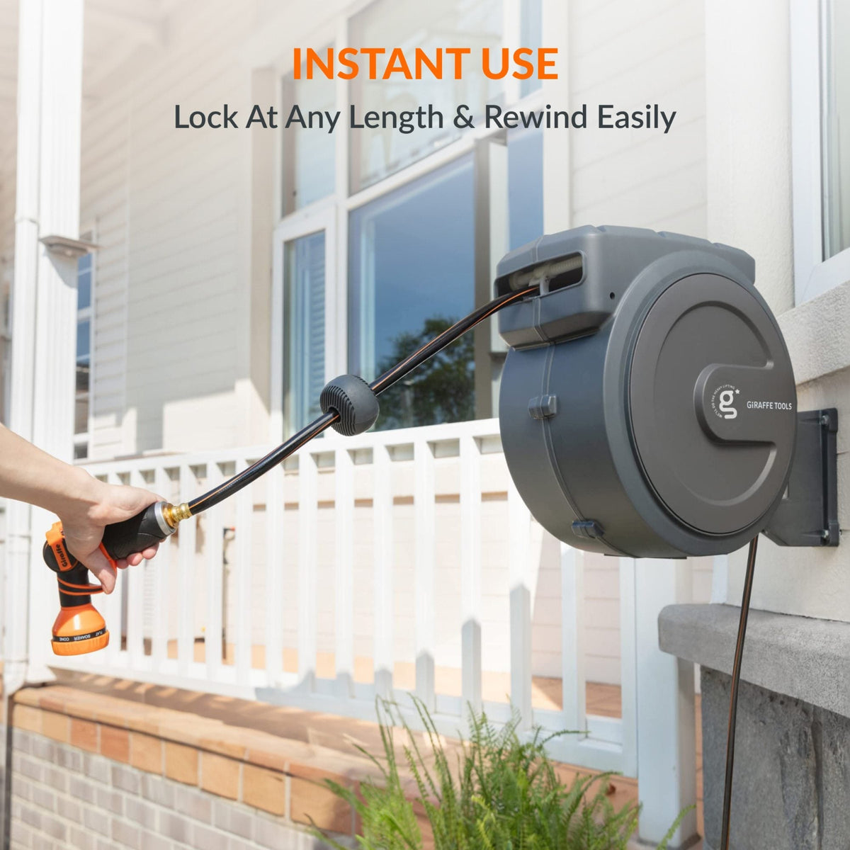 Wall-mounted retractable hose reel with a nozzle attached, set against a house exterior showing feature of lock at any length and rewind easily.